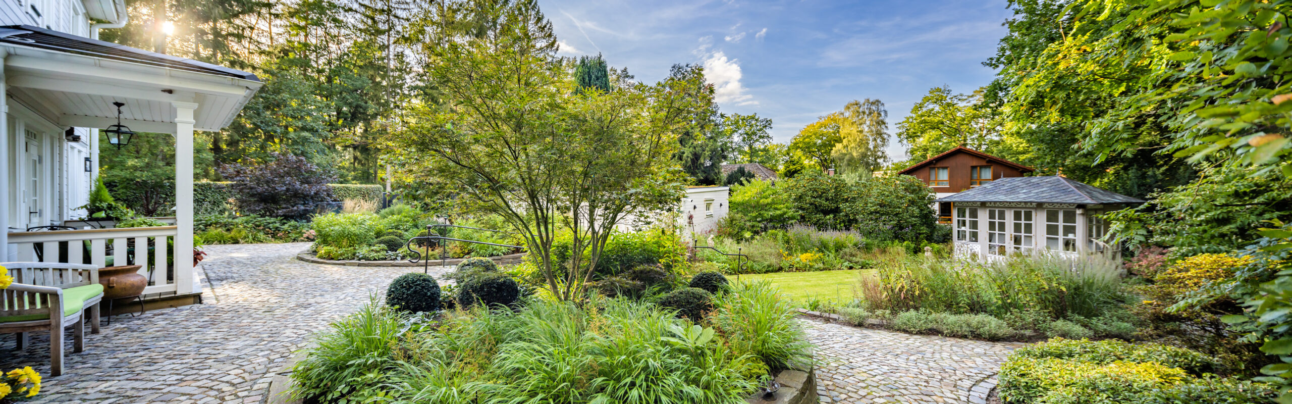 Gartenlandschaft mit Wegen und Pflanzen Garten mit gepflasterten Wegen, Büschen und verschiedenen Pflanzen in einer grünen Umgebung.