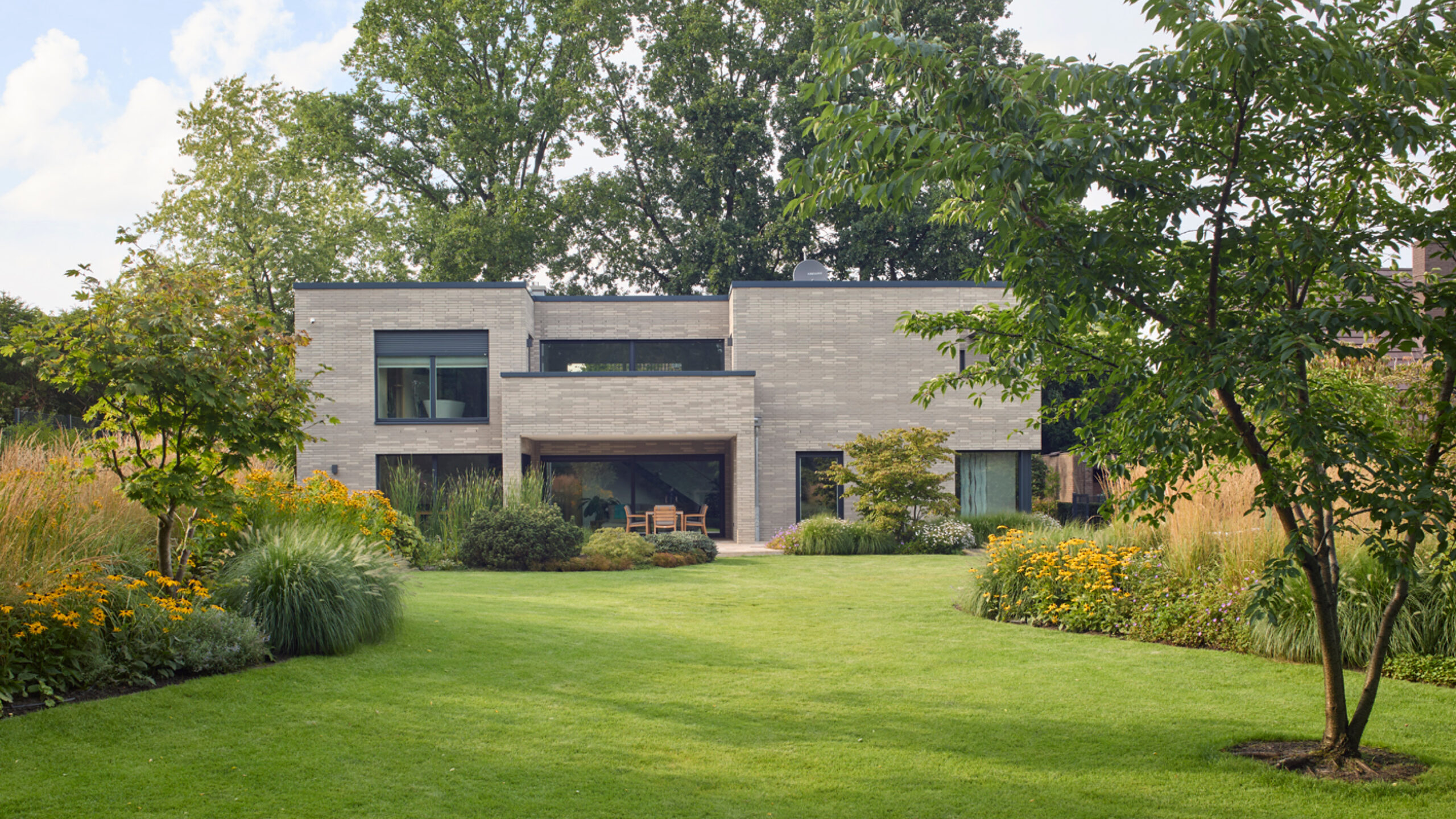 Moderne Wohnhausansicht mit Garten Moderne Wohnhausansicht mit großen Fenstern und einem gepflegten Garten im Vordergrund.