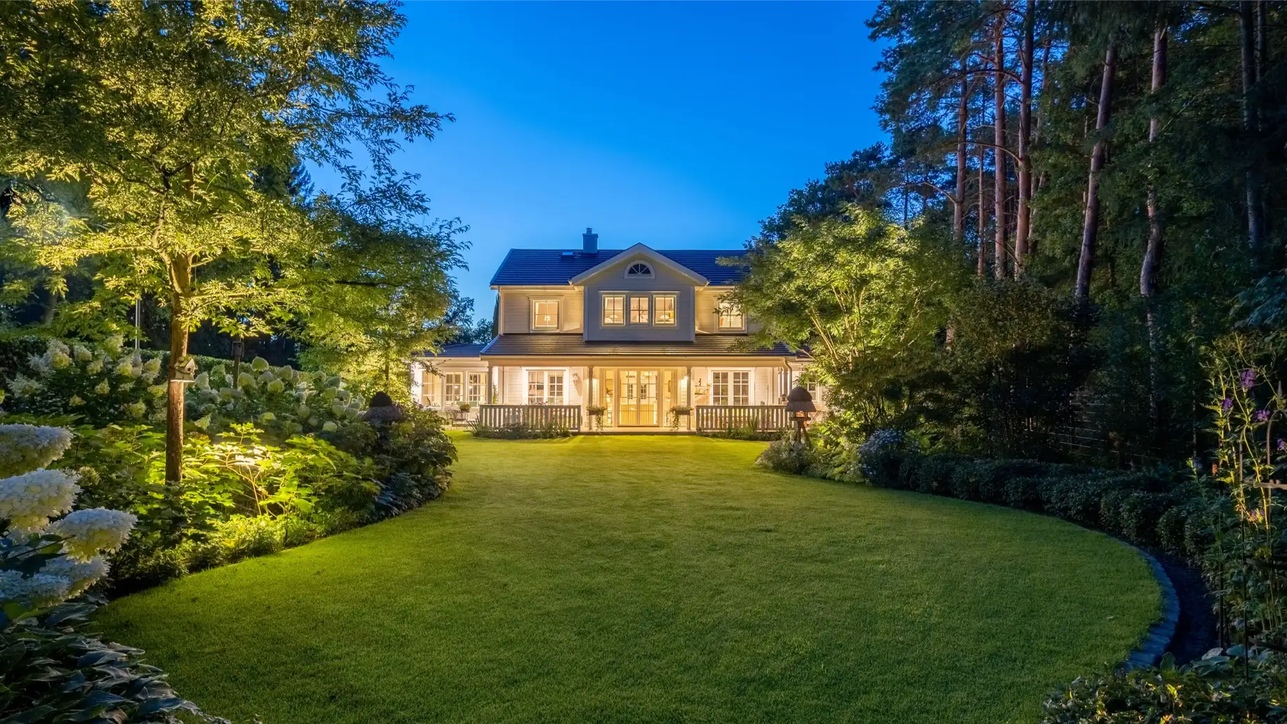 Ein zweigeschossiges Haus mit beleuchtetem Garten und Bäumen bei Nacht.