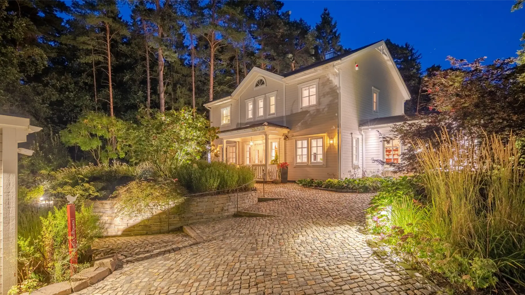 Helles Einfamilienhaus mit großen Fenstern und einem gepflegten Garten bei Nachtbeleuchtung.