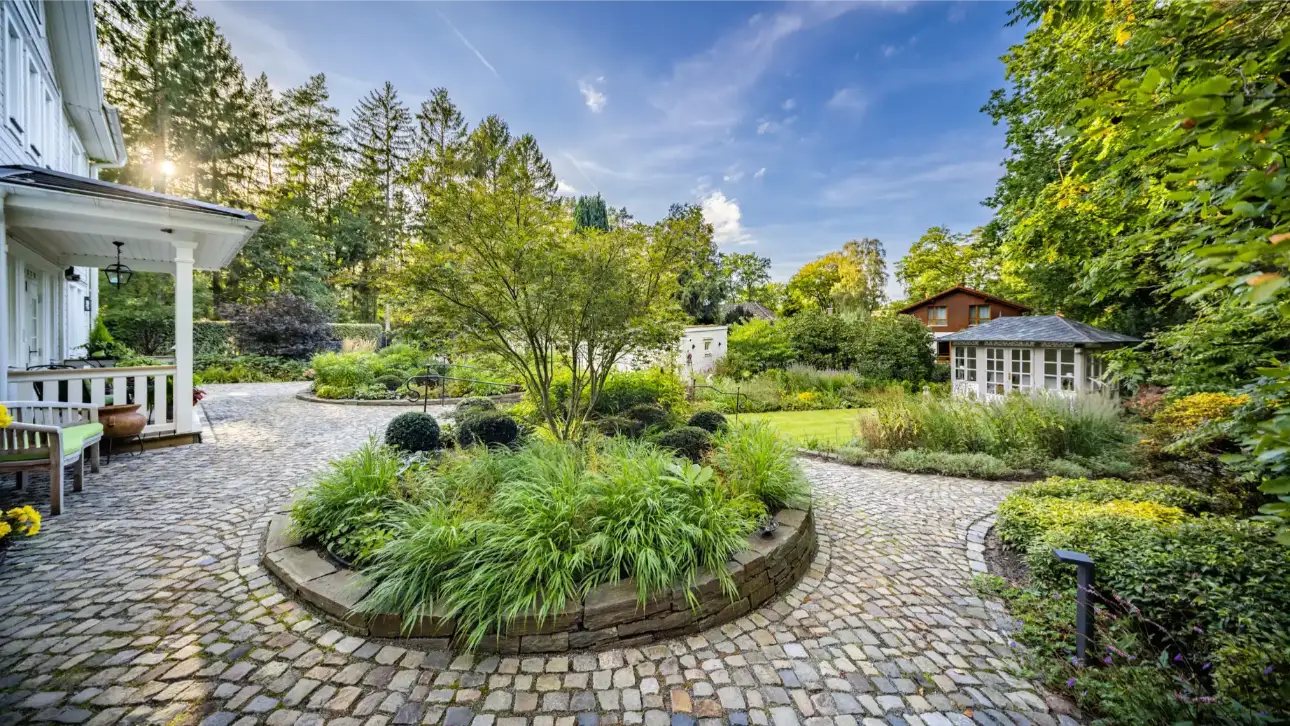 Garten mit gepflastertem Weg, Bäumen und verschiedenen Pflanzen in einer ruhigen Umgebung.
