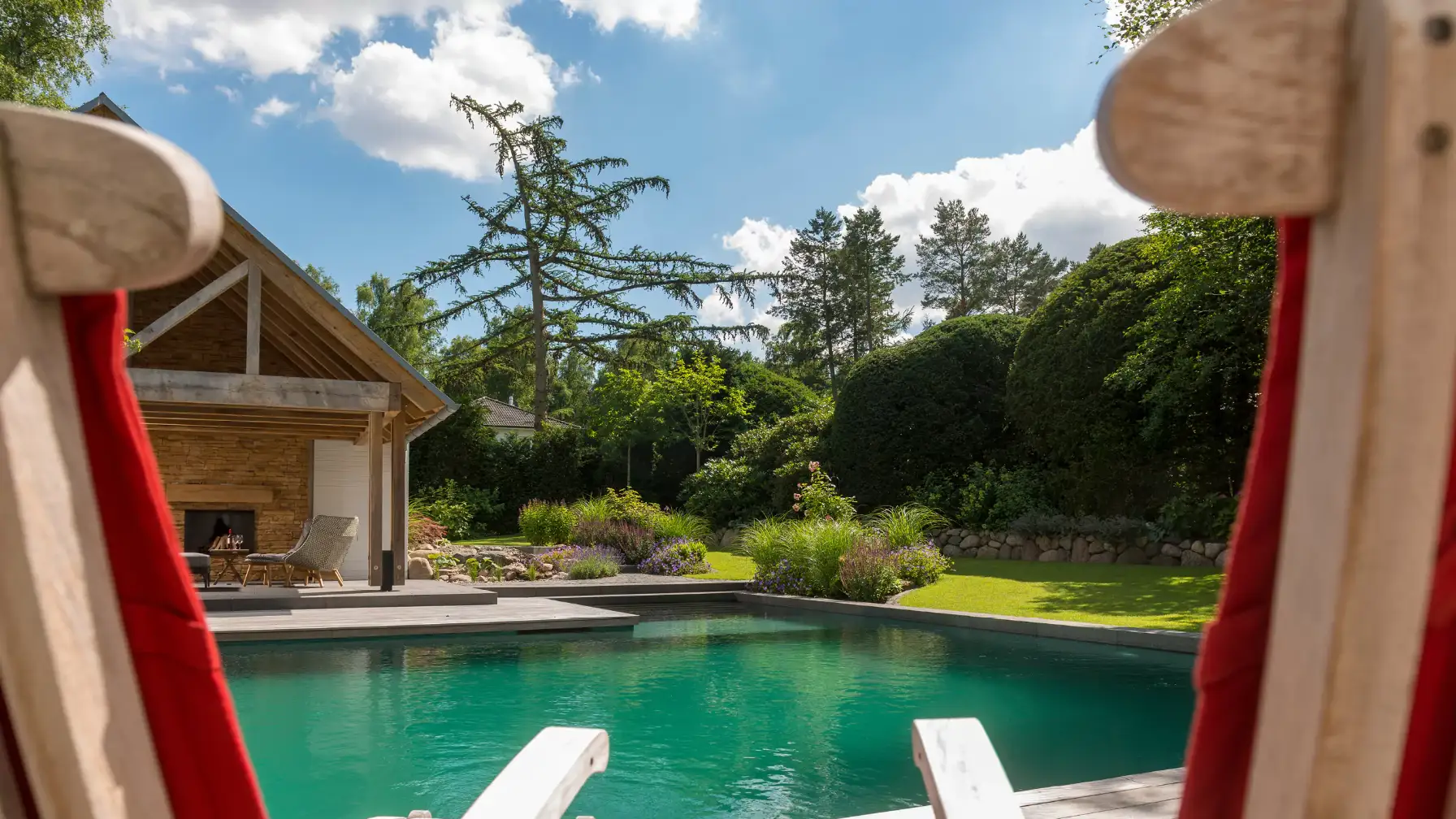 Ein Schwimmbad mit Liegestühlen und einer gepflegten Gartenlandschaft im Hintergrund.