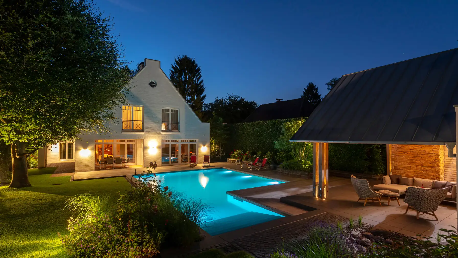 Ein modernes Haus mit beleuchtetem Pool und Garten bei Nacht.