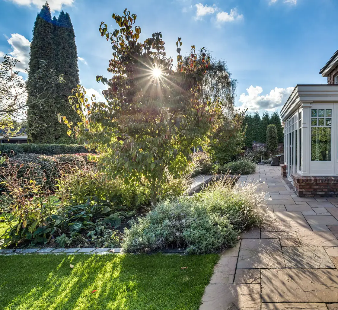 Beran Gärten, Herbstgarten mit Terrasse und Wintergarten im warmen Sonnenlicht Moderne weiße Villa mit großen Fenstern und einem gepflegten Garten im Vordergrund.