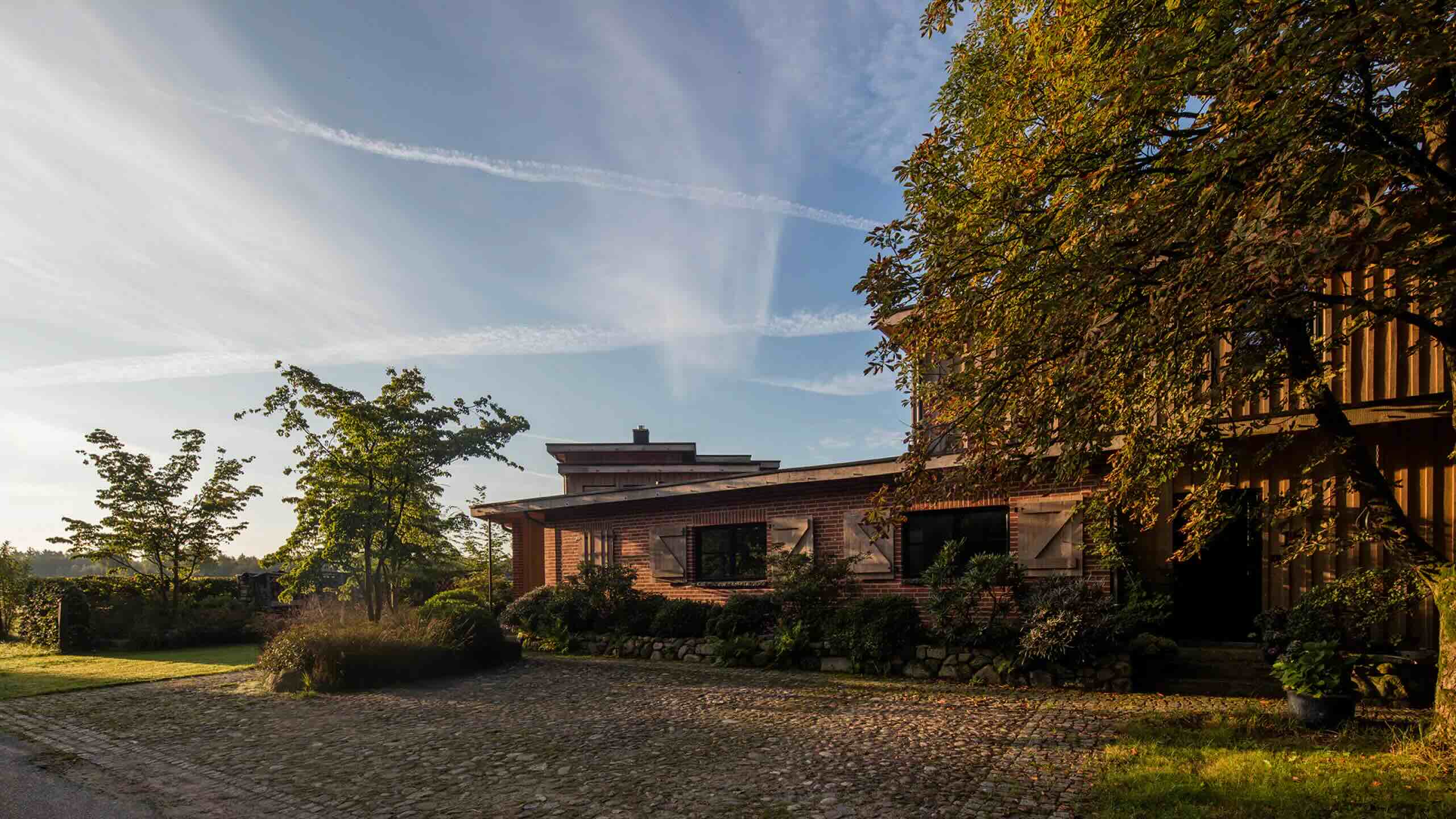 Im warmen Abendlicht liegen Kopfsteinpflaster, rote Backsteinfassaden und herbstliche Bäume rund um den ruhigen Hof von Beran Gärten.